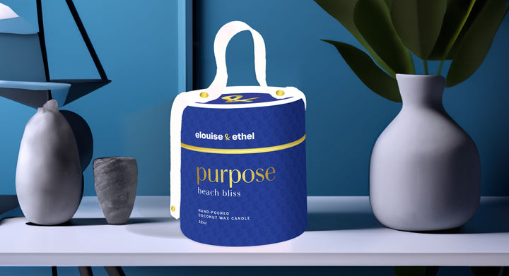 Purpose candle sitting on a white table next to a plant in a white pot in front of a blue wall